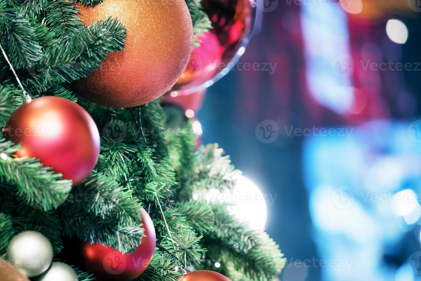 avvicinamento di rosso fronzolo sospeso a partire dal un' decorato Natale albero su sfocato di luci con decorato albero, scintillante e bokeh sfondo. copia spazio per il tuo testo. foto