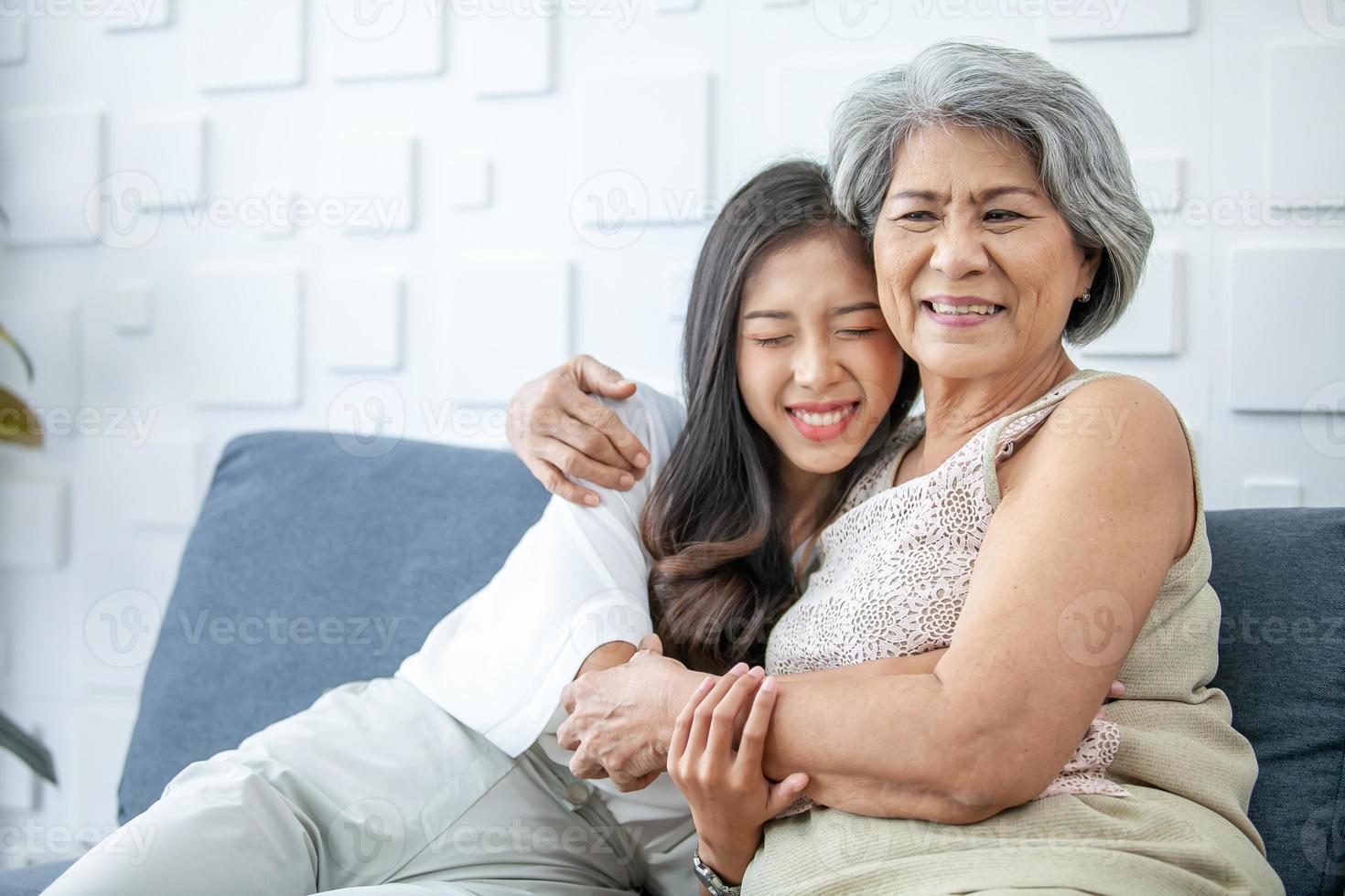 asiatico nonna e nipotina abbracciato con contento umore su il divano nel casa. foto