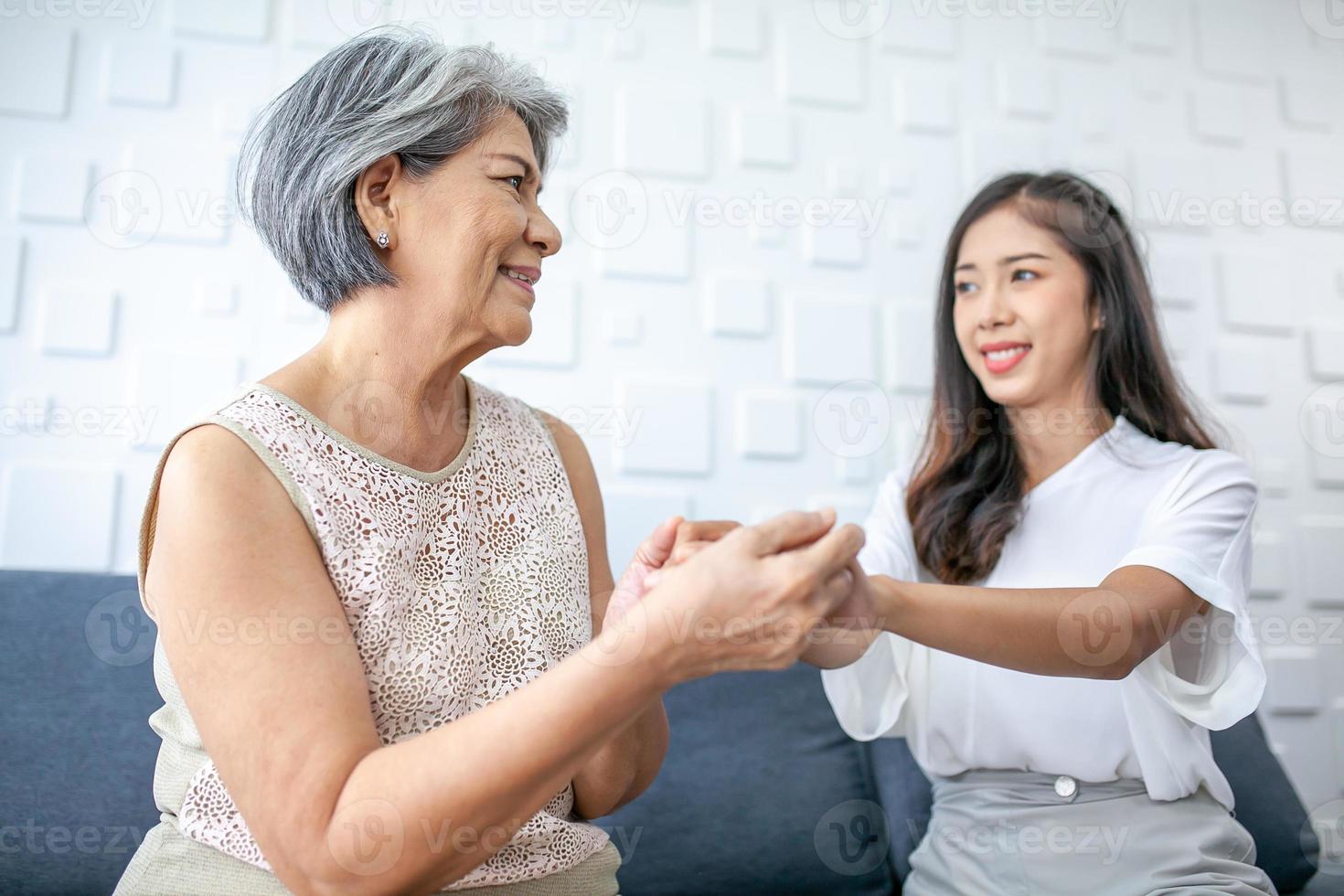 asiatico giovane e anziano donna, nonna e nipotina Tenere mani per supporto e amore con sorrisi su il divano nel il Casa. foto