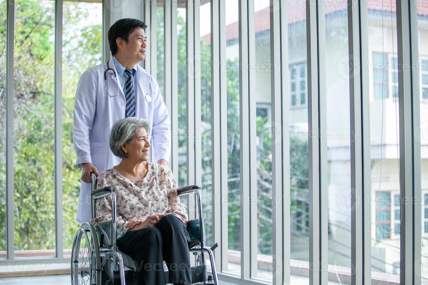 asiatico medico supporto e applauso su anziano paziente nel sedia a rotelle parlando, sorridente nel comfort a casa. assistenza sanitaria e medicina concetto. foto