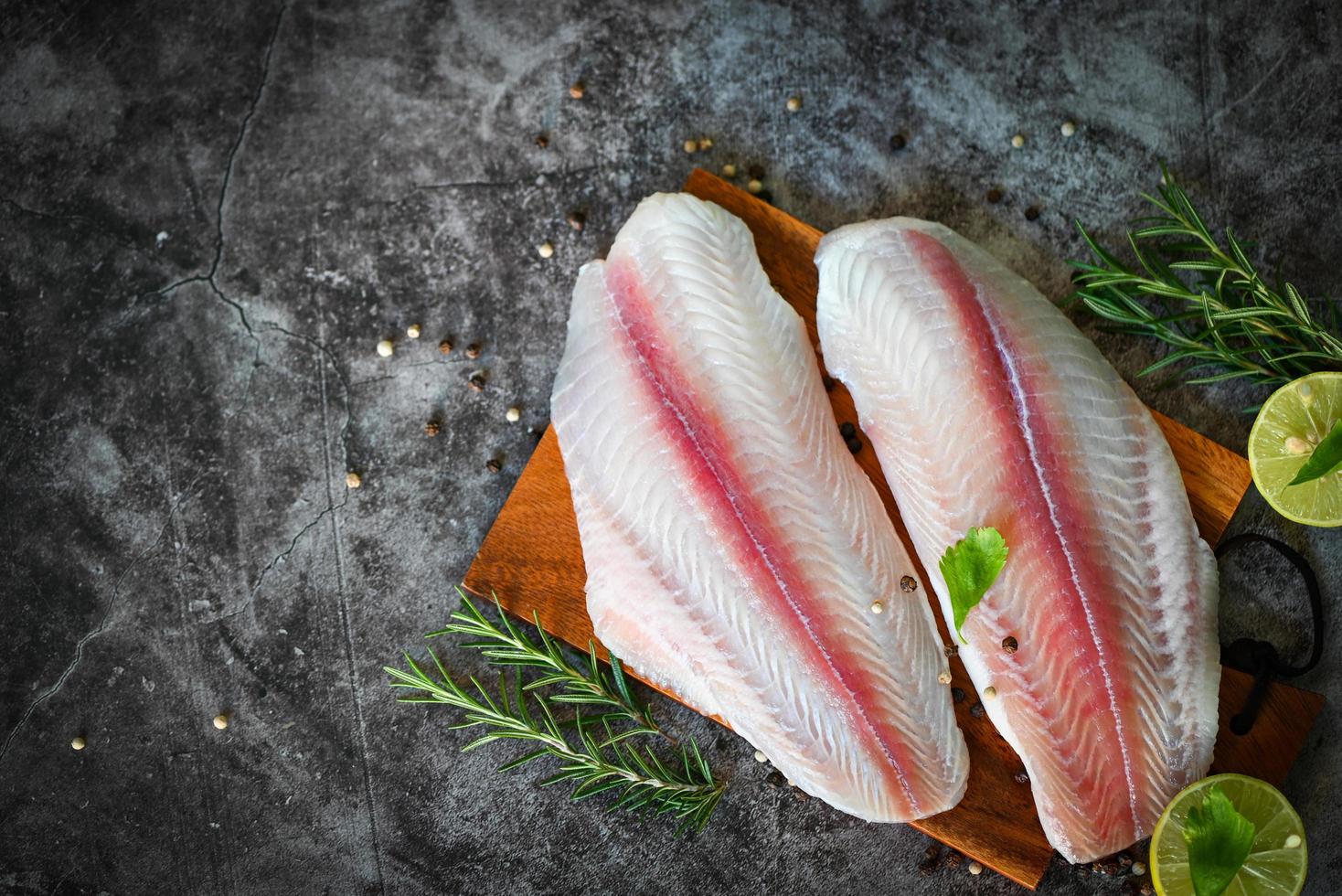 pesce filetto su di legno tavola con ingredienti per cucinando, carne dolly pesce Tilapia a strisce pesce gatto, fresco crudo pangasio pesce filetto con erba e spezie nero Pepe Limone lime foto