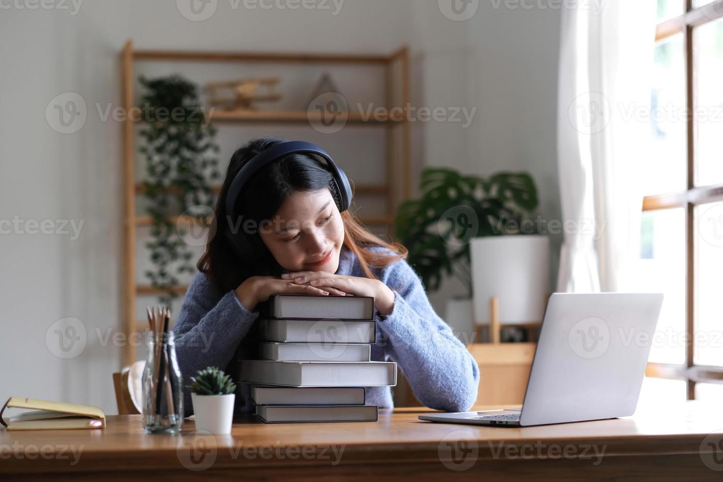 sorridente studentessa universitaria asiatica studentessa studia in biblioteca con libri per laptop facendo ricerche online per i corsi, prendendo appunti per l'assegnazione dei compiti a casa, concetto di e-learning per l'istruzione online foto