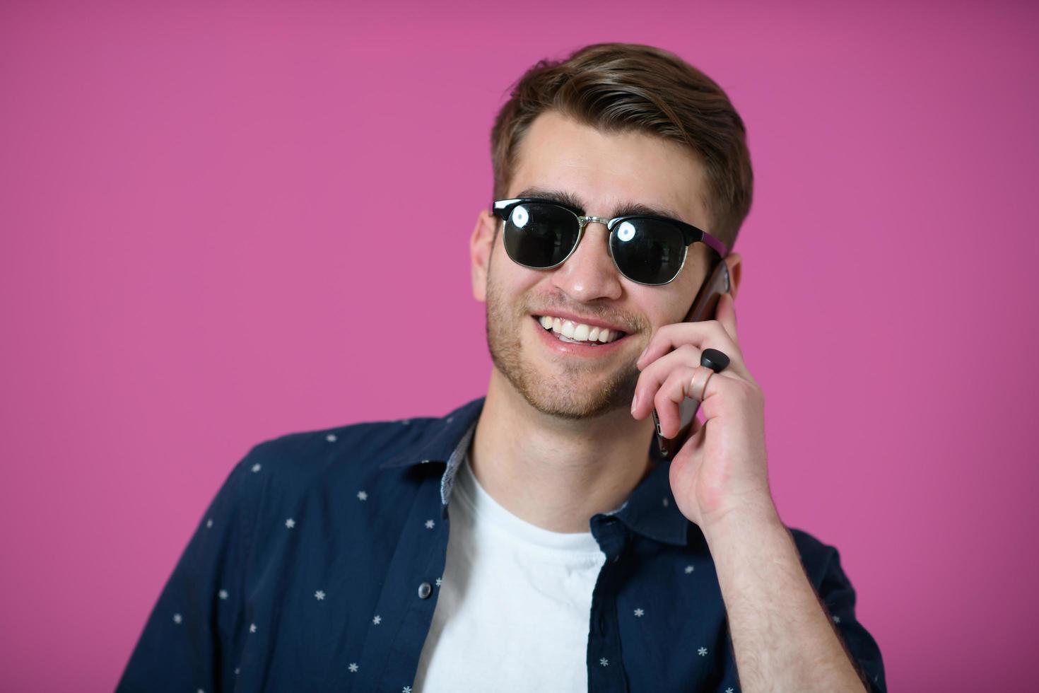 un' giovane uomo indossare un' blu camicia e occhiali da sole utilizzando un' smartphone foto