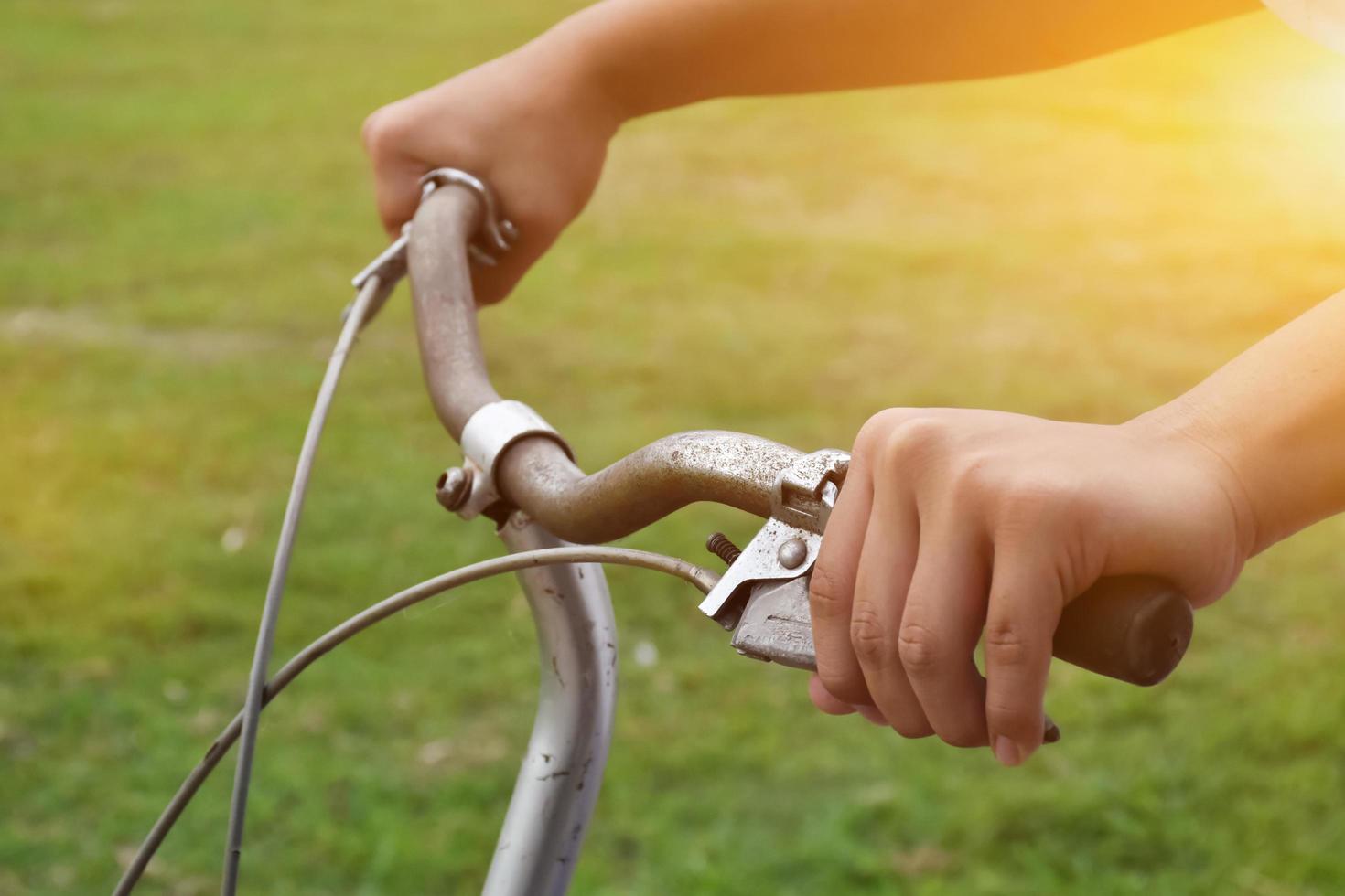 un' giovane tipo detiene maniglia barre di Vintage ▾ bicicletta quale parcheggiata su il prato sfondo, morbido e selettivo messa a fuoco su mano. foto