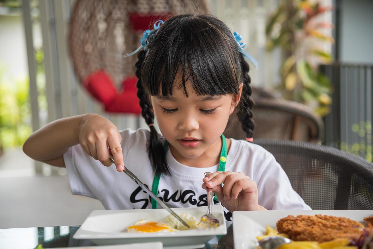 poco ragazza asiatico mangiare fritte uovo su piatto a tavolo. foto