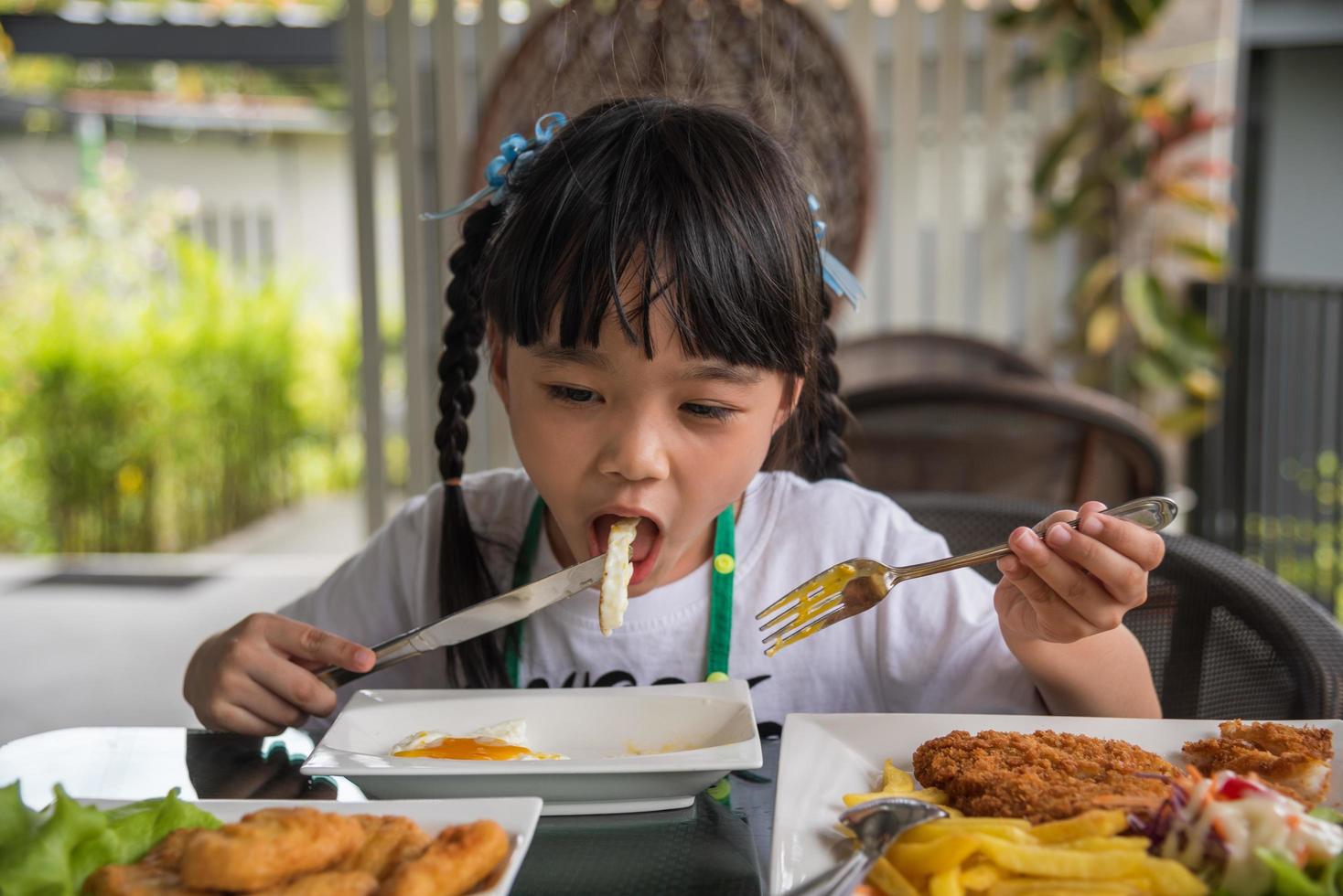 poco ragazza asiatico mangiare fritte uovo su piatto a tavolo. foto