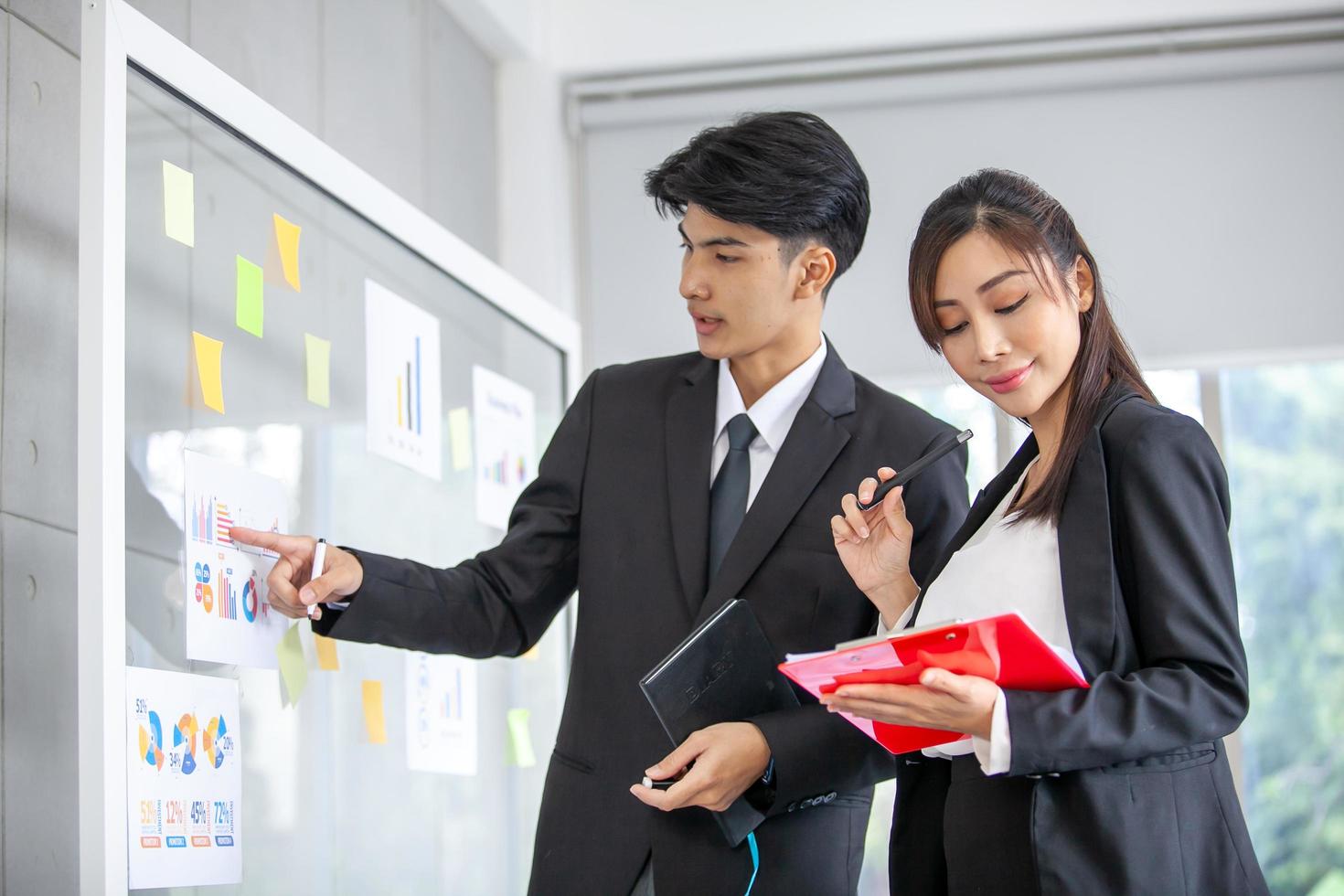 uomini d'affari che si incontrano in ufficio e usano post-it per condividere un'idea. uomo d'affari e imprenditrice mettendo note adesive colorate sulla finestra di vetro in ufficio. foto