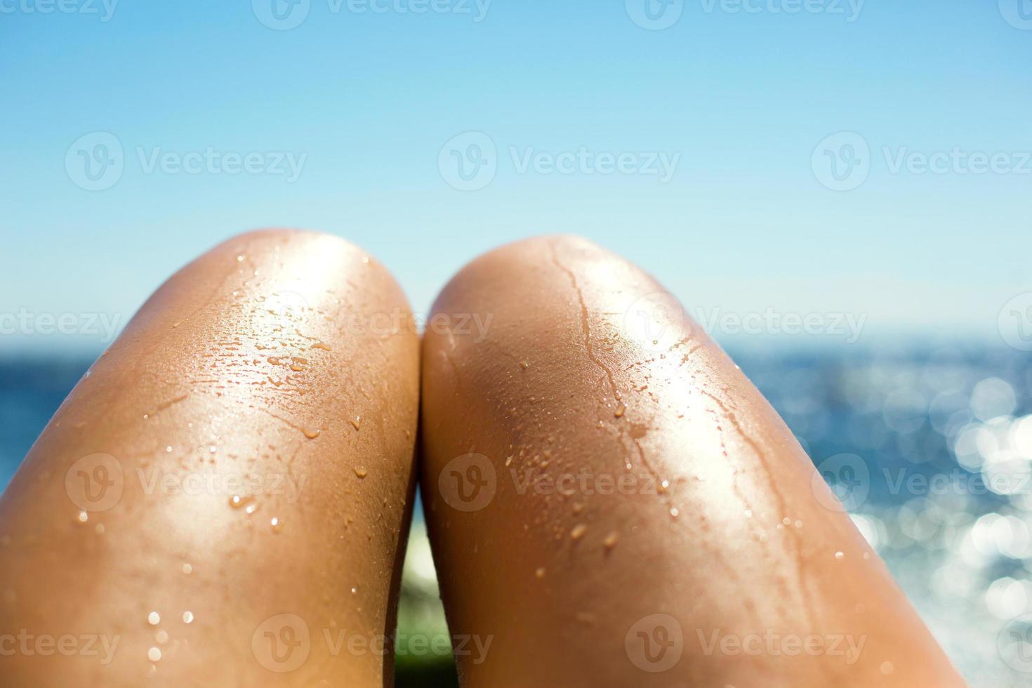 gambe femminili abbronzate lisce negli spruzzi d'acqua sulla spiaggia sullo sfondo del mare. prodotti abbronzanti, protezione solare, cura della pelle, depilazione, vacanze al mare. copia spazio foto