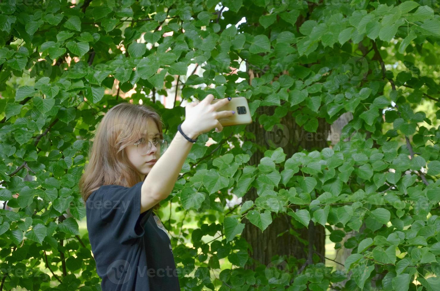 una ragazza si fotografa con il telefono vicino agli alberi foto