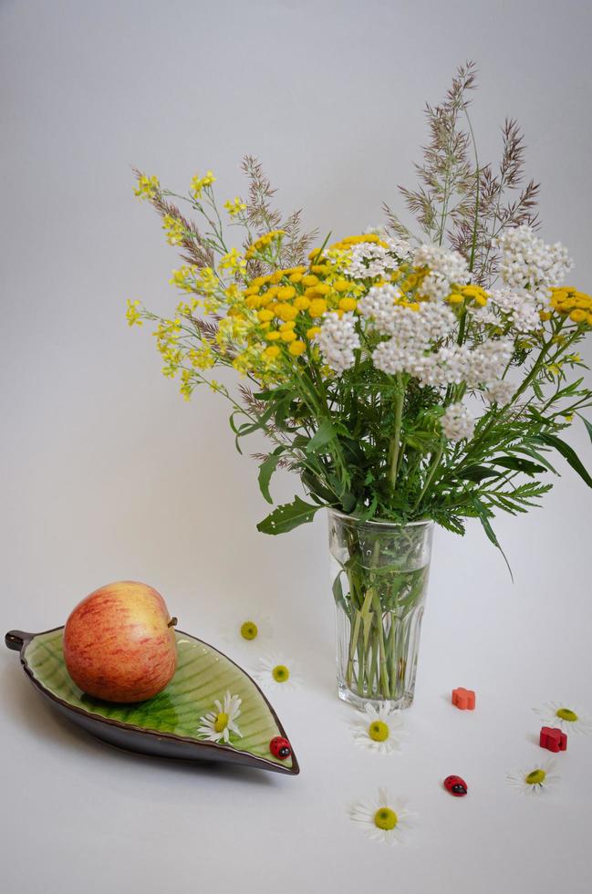 natura morta di fiori di campo e una mela su un piattino, il tutto su uno sfondo chiaro foto