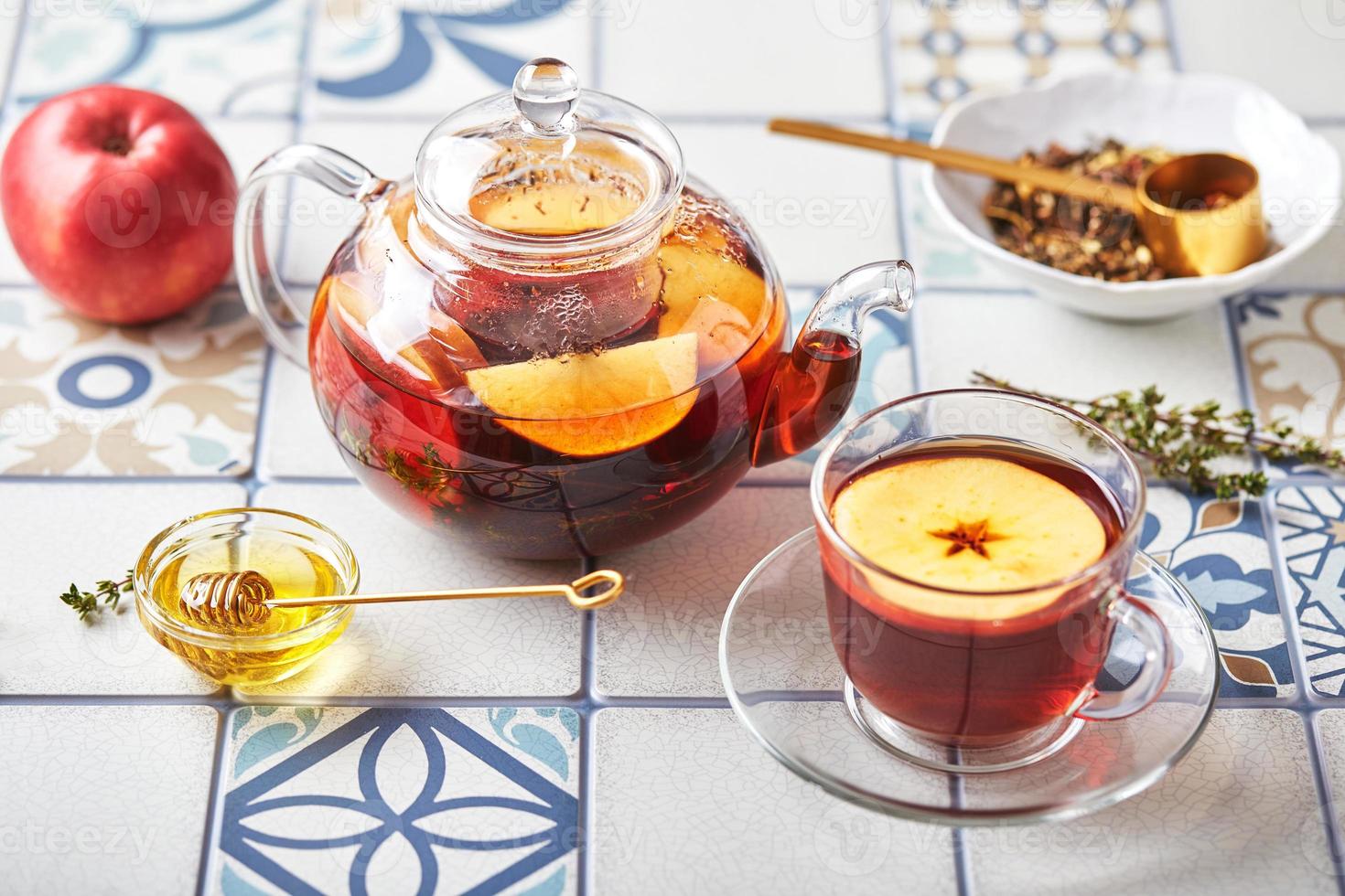 frutta tè con mele e timo nel bicchiere teiera e tazza su tavolo fatto di colorato piastrelle foto