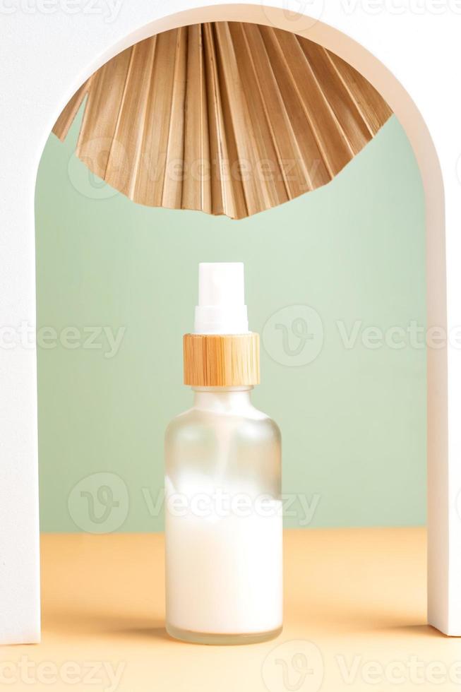 bianca smerigliato bicchiere bottiglia di naturale viso idratante crema su beige sfondo nel bianca arco decorato con asciutto palma foglia. eco cosmetici concetto. foto