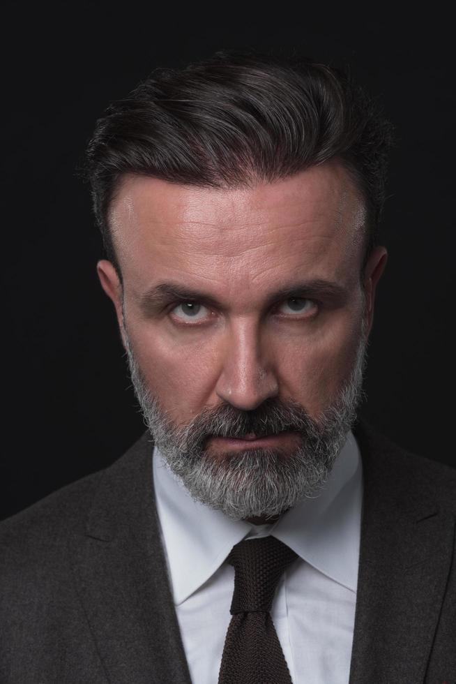 ritratto di un' elegante elegante anziano uomo d'affari con un' barba e casuale attività commerciale Abiti nel foto studio isolato su buio sfondo Esprimere a gesti con mani