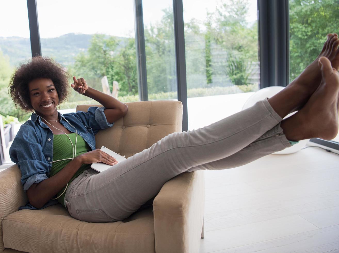africano americano donna a casa nel sedia con tavoletta e testa telefoni foto