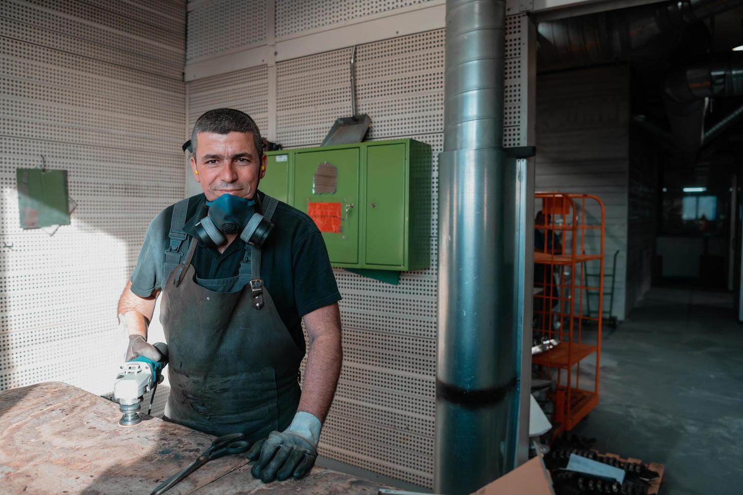 interno di una fabbrica di ingegneria dell'industria pesante con un lavoratore industriale che utilizza una smerigliatrice angolare e taglia un tubo di metallo. appaltatore in uniforme di sicurezza e elmetto per la produzione di strutture metalliche. foto