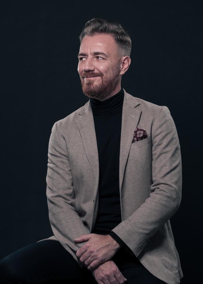 ritratto di adulto uomo d'affari indossare di moda completo da uomo e seduta nel moderno studio su elegante sedia contro il nero sfondo foto