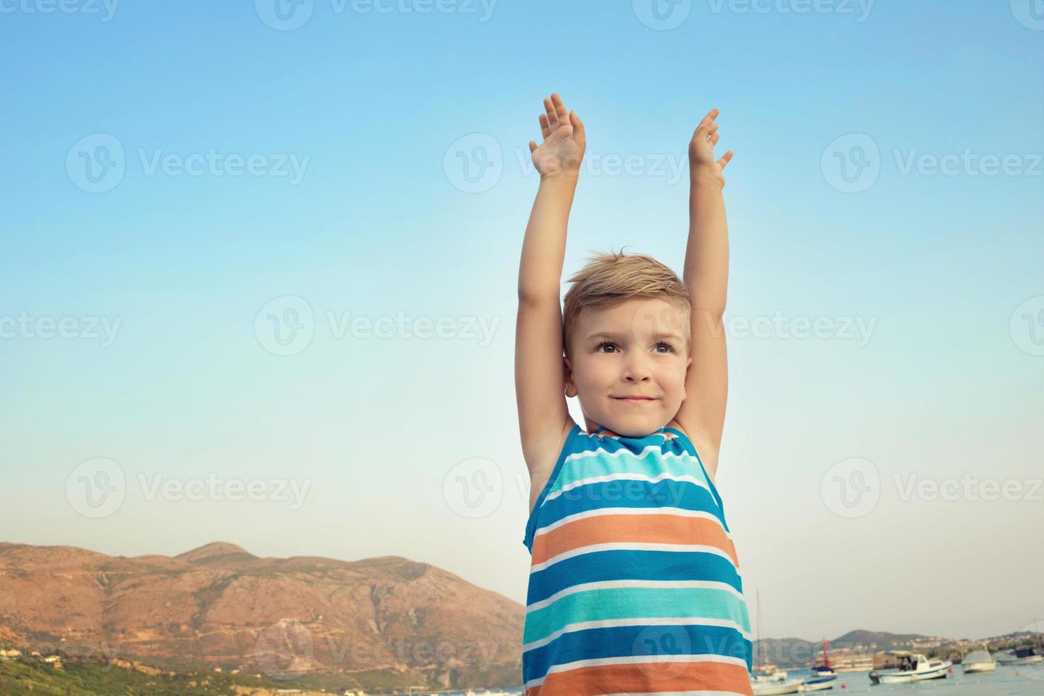 piccolo ragazzo con sollevato braccia su spiaggia. foto