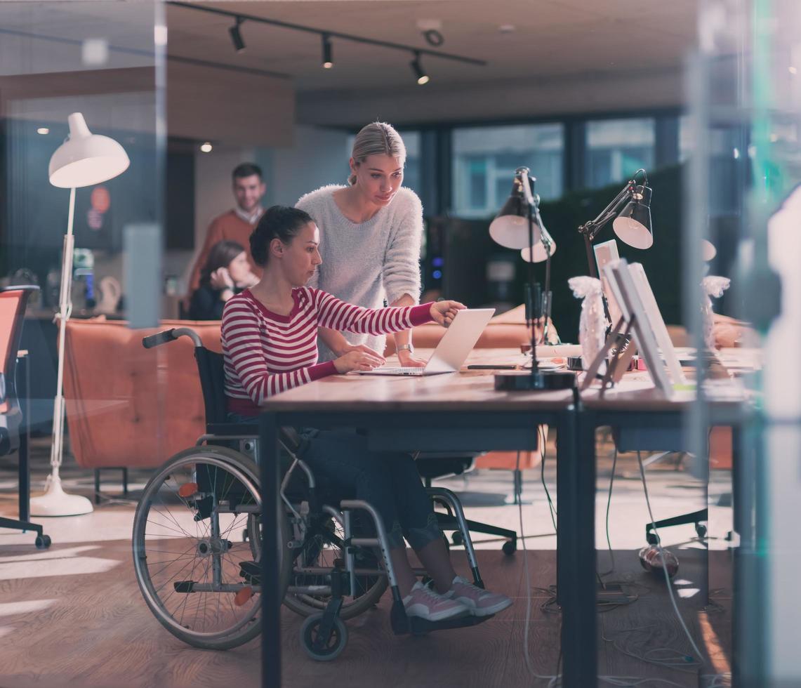 Disabilitato donna d'affari nel un' sedia a rotelle nel moderno coworking ufficio spazio. colleghi nel sfondo. invalidità e handicap concetto. selettivo messa a fuoco foto