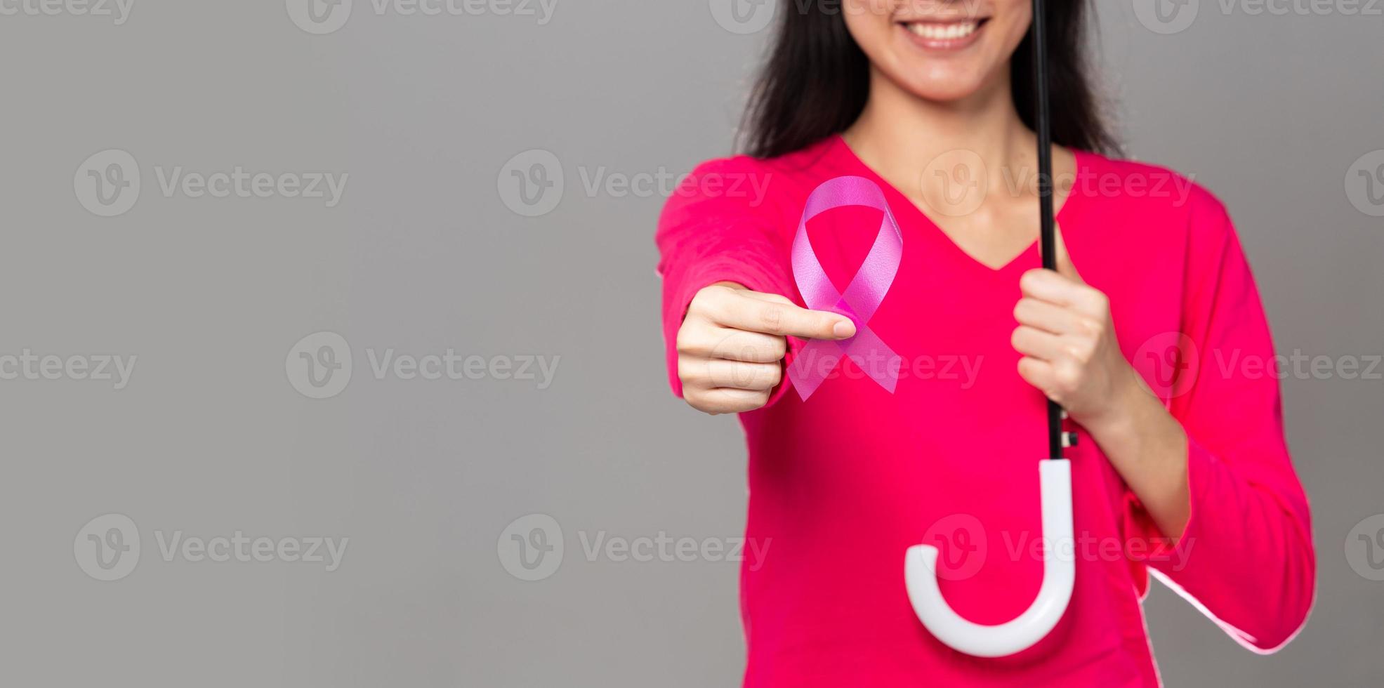 ottobre Seno cancro consapevolezza mese, adulto donna nel rosa vestito mano Tenere rosa nastro e ombrello per supporto protezione. internazionale donne, madre e mondo cancro giorno concetto copia spazio foto