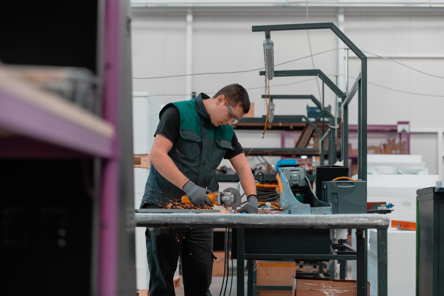 interno di una fabbrica di ingegneria dell'industria pesante con un lavoratore industriale che utilizza una smerigliatrice angolare e taglia un tubo di metallo. appaltatore in uniforme di sicurezza e elmetto per la produzione di strutture metalliche. foto