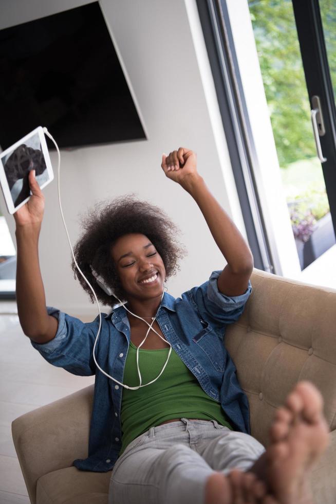 africano americano donna a casa nel sedia con tavoletta e testa telefoni foto