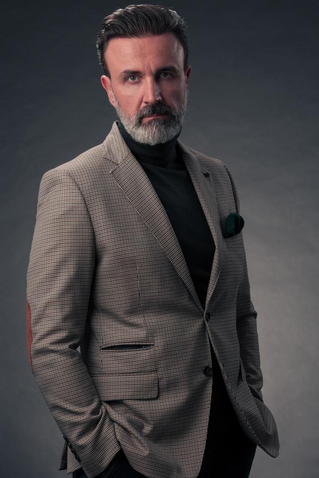 ritratto di un' elegante elegante anziano uomo d'affari con un' barba e casuale attività commerciale Abiti nel foto studio isolato su buio sfondo Esprimere a gesti con mani