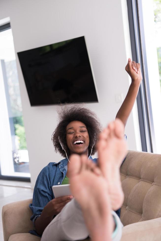 africano americano donna a casa nel sedia con tavoletta e testa telefoni foto