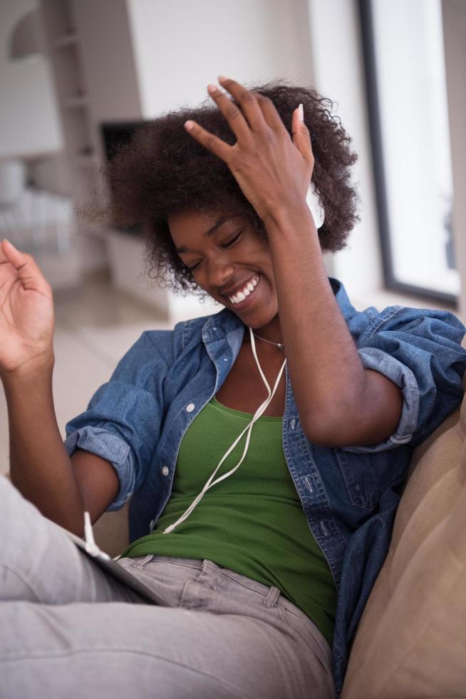 africano americano donna a casa nel sedia con tavoletta e testa telefoni foto