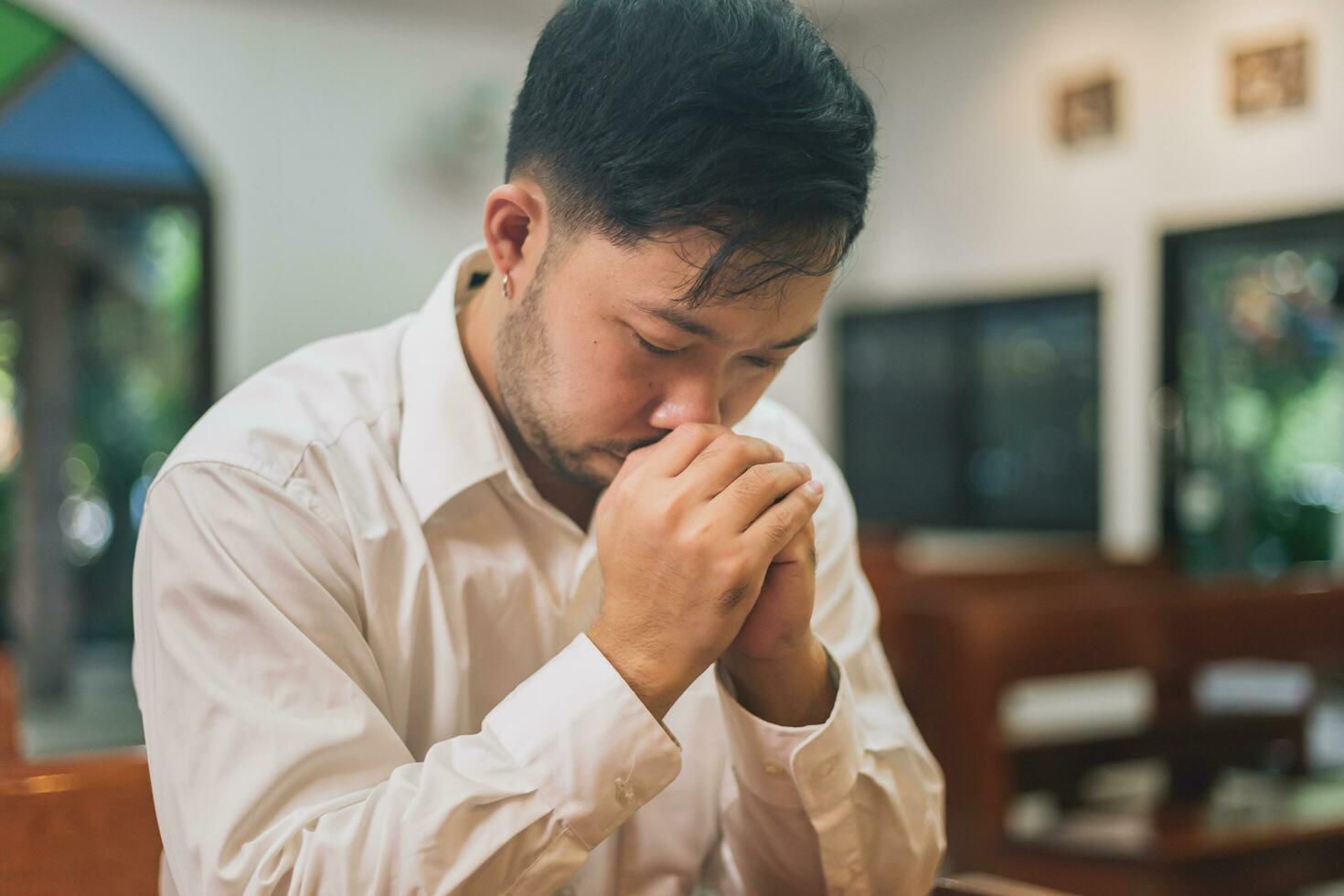 calma pieno di speranza uomo preghiera pregare Cristo. tranquillo, calmo spirituale religioso preghiera utilizzando attraversare culto Gesù. asiatico bello uomo credere Dio cattolico preghiera culto Dio vicino occhi piegato mani e dita. foto