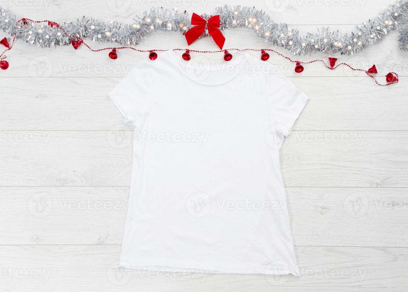 vicino su bianca vuoto modello t camicia con copia spazio e Natale vacanza concetto. superiore Visualizza modello maglietta e rosso arco su bianca di legno sfondo. contento nuovo anno decorazioni Accessori. natale attrezzatura foto