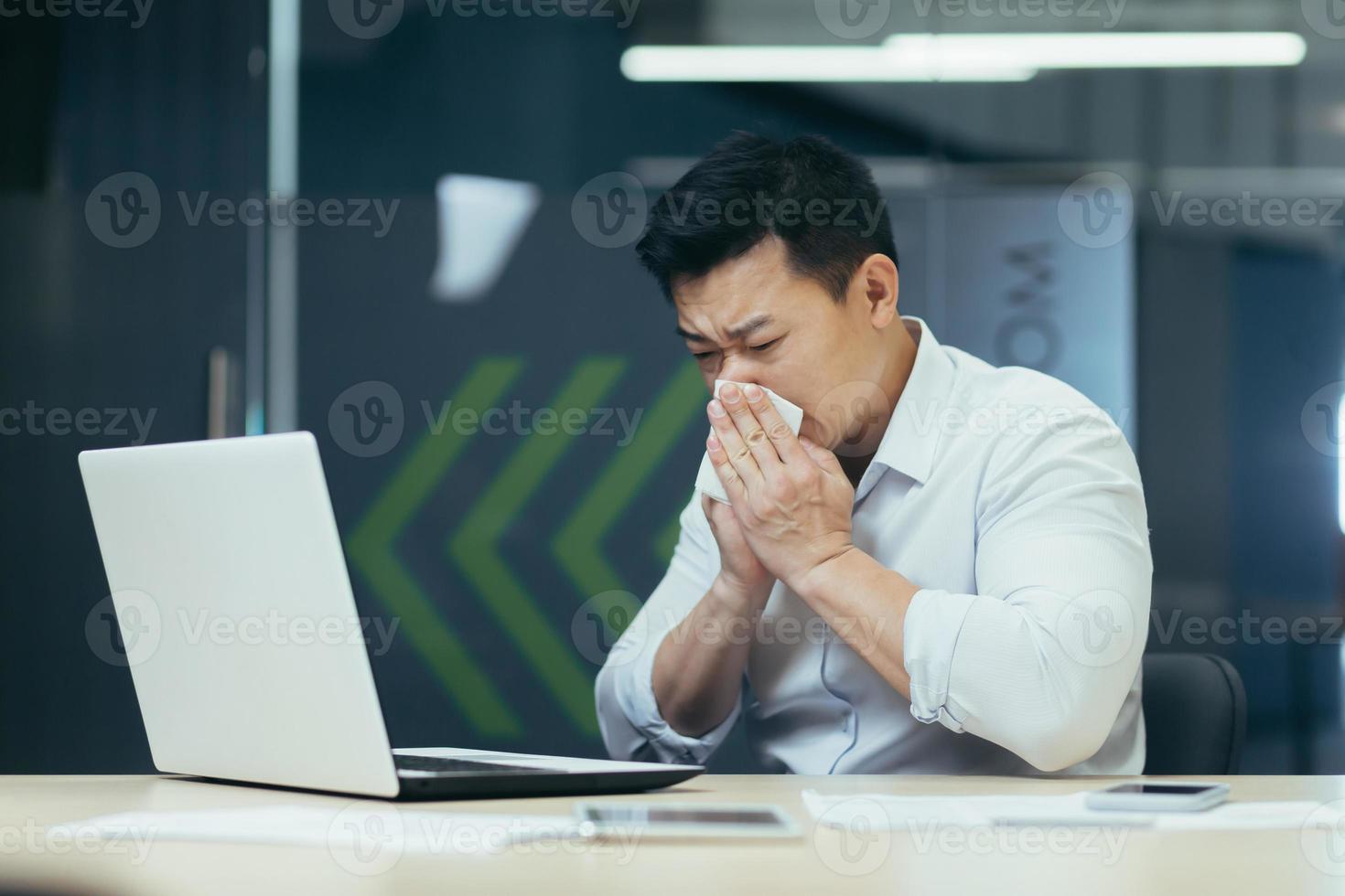 malato uomo nel ufficio tosse e che cola naso, asiatico uomo d'affari con freddo lavori nel ufficio su il computer portatile foto