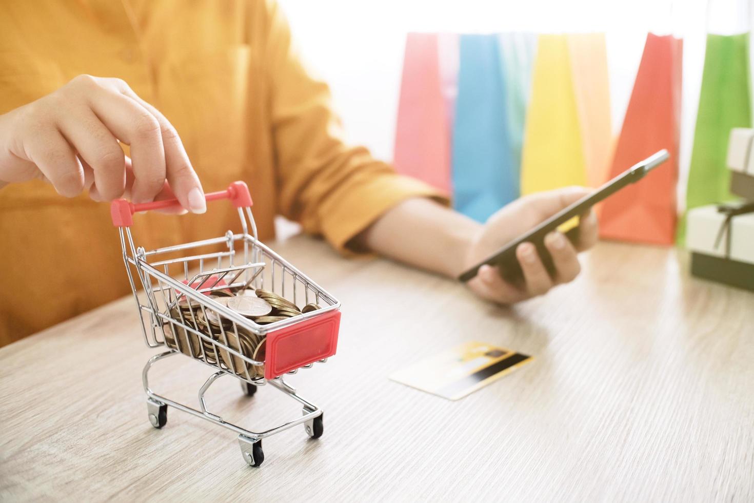 shopping online donna con smartphone in possesso di un piccolo carrello foto