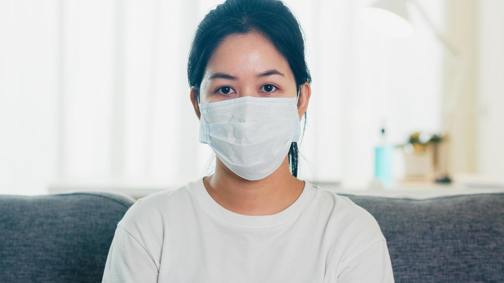 donna asiatica che indossa una maschera protettiva seduto sul divano. foto