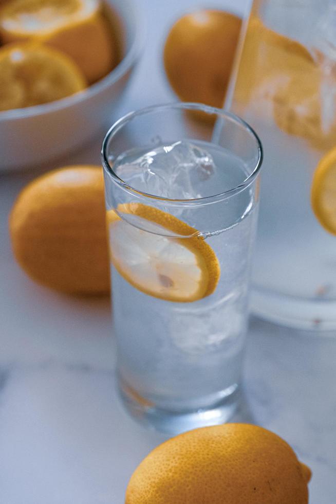 alto bicchiere d'acqua tra limoni freschi foto