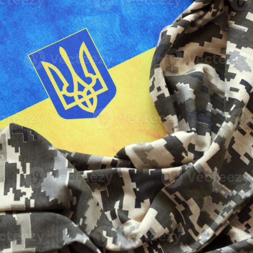 ucraino bandiera e cappotto di braccia con tessuto con struttura di pixeled camuffare. stoffa con Camo modello nel grigio, Marrone e verde pixel forme con ucraino tridente cartello foto