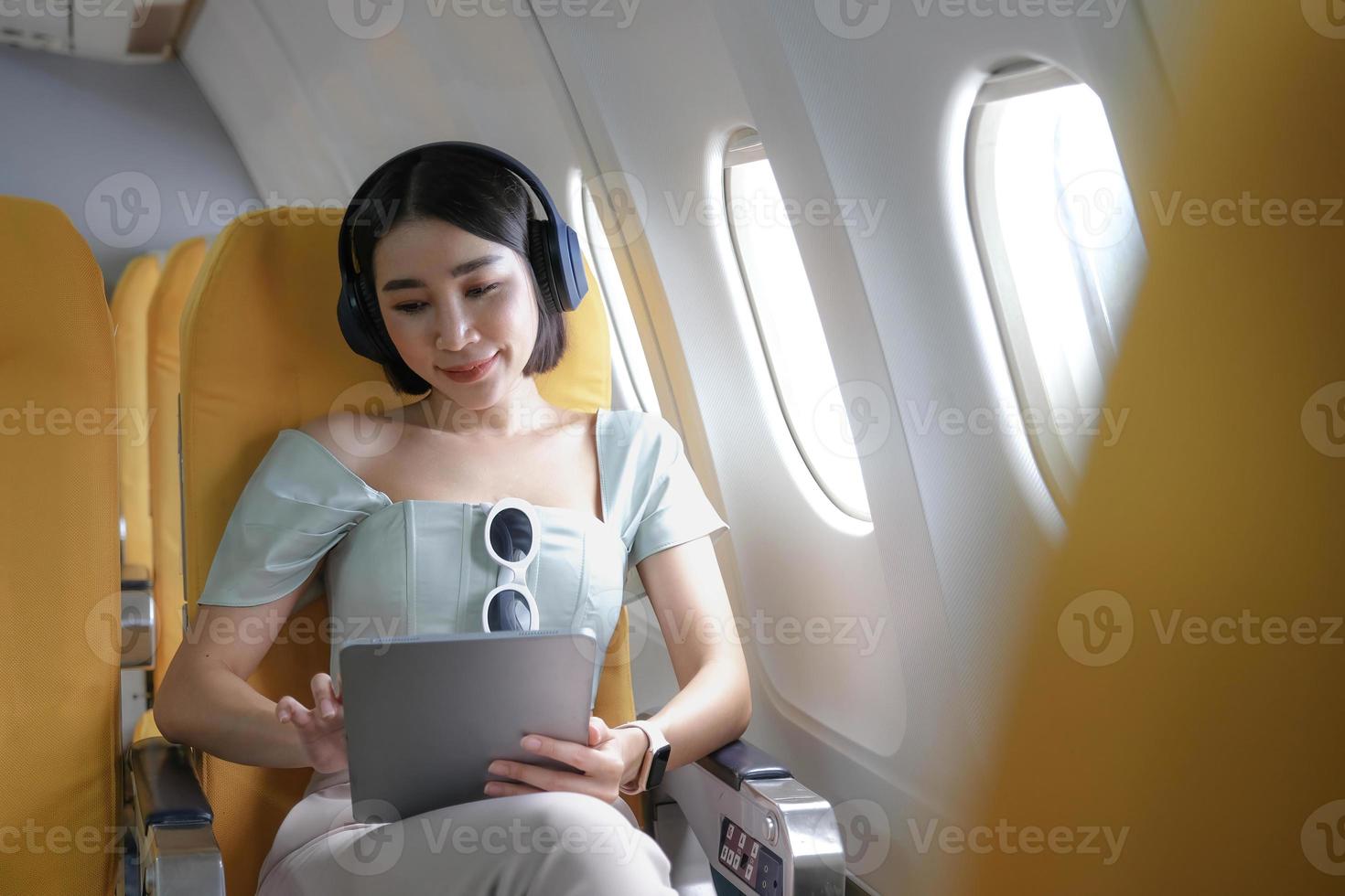viaggio turismo con moderno tecnologia e aria voli concetto, donna seduta nel aereo con moderno digitale aggeggio e ricerca preferito musica elenco di riproduzione nel applicazione per ascoltando foto