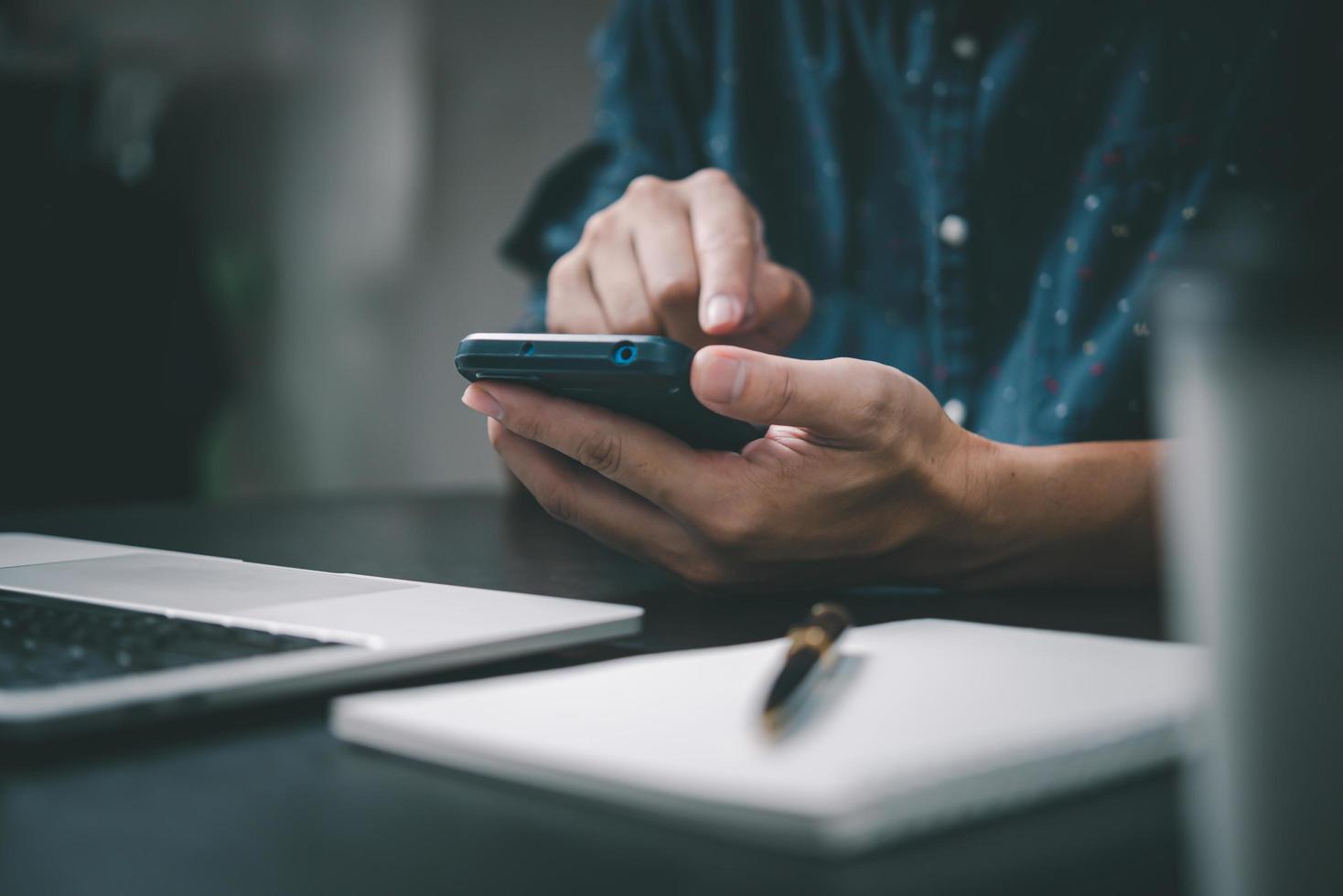 uomo Tenere un' Telefono con un' penna e carta per Scrivi un' Nota nel un ufficio diario utilizzando un' il computer portatile a ufficio. foto