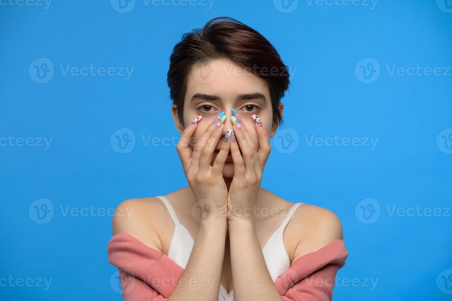 magro carino adolescenziale ragazza nascondiglio inferiore viso nel sua mani, blu sfondo foto