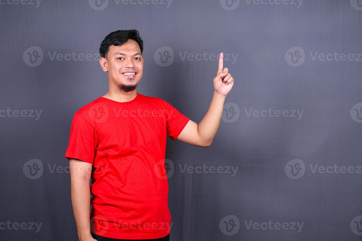 asiatico giovane uomo nel rosso maglietta puntamento con il suo dito isolato su grigio sfondo foto