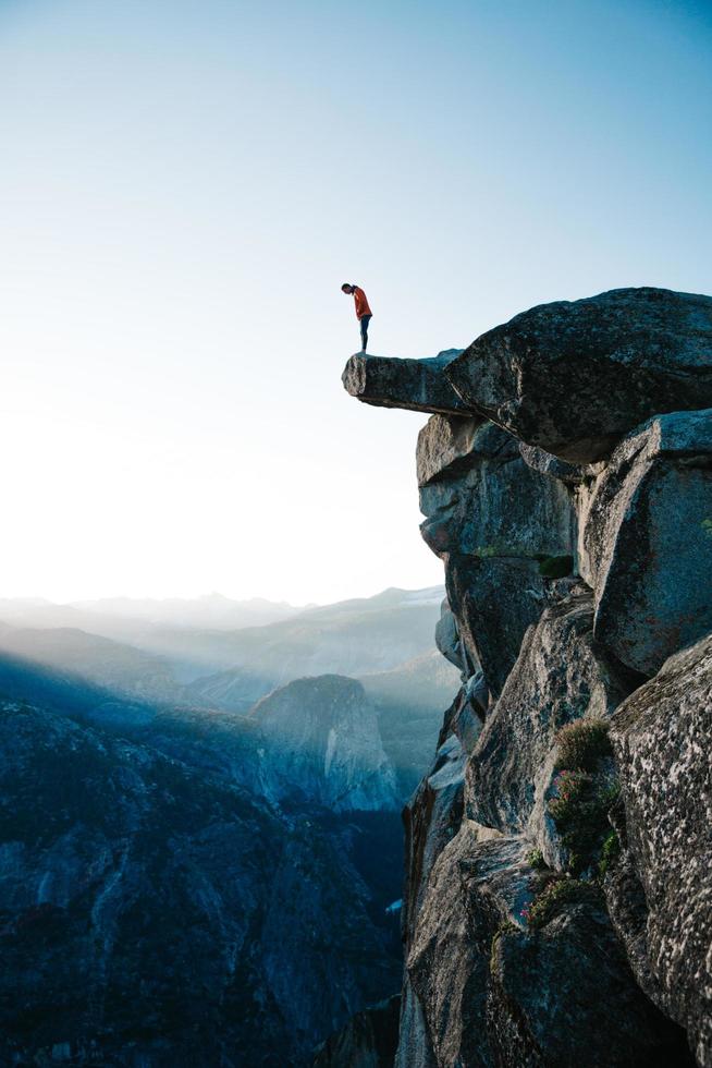 uomo in piedi sulla scogliera che si affaccia su Yosemite foto
