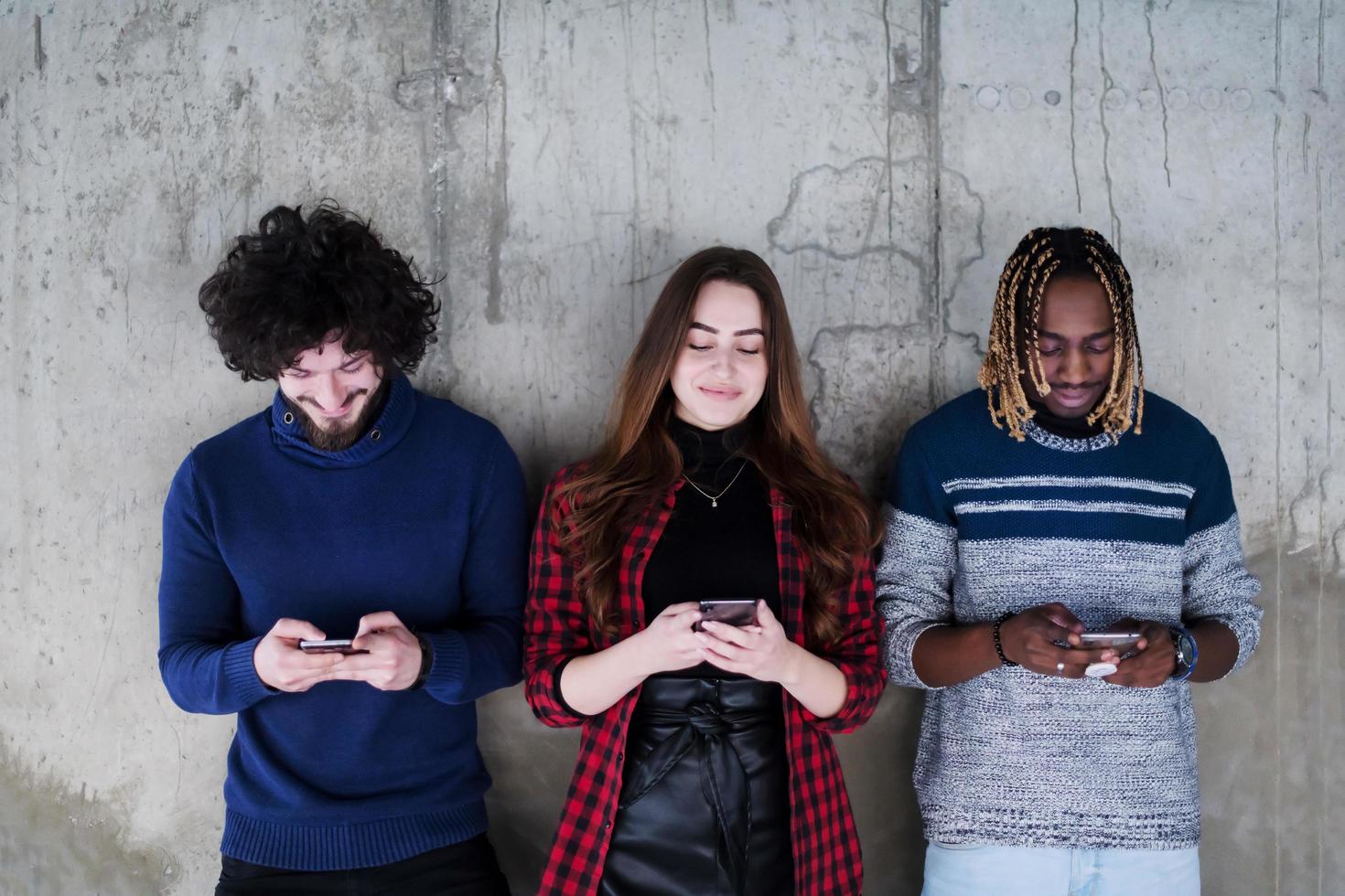 casuale multietnico attività commerciale squadra utilizzando mobile telefoni nel davanti di un' calcestruzzo parete foto