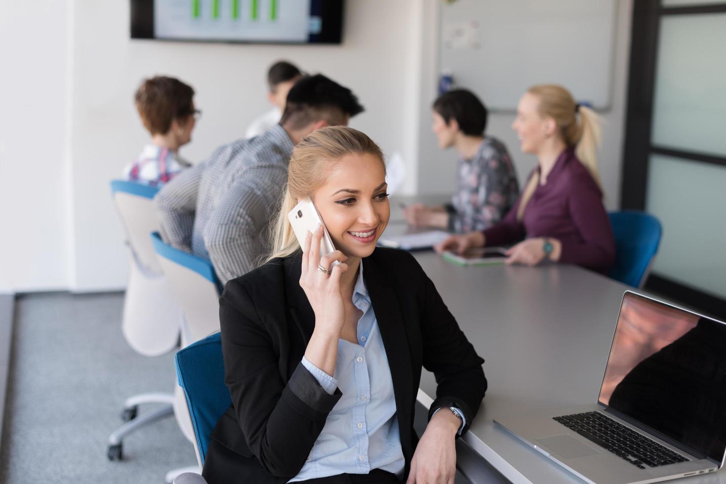 attività commerciale donna parlando su Telefono a ufficio con squadra su incontro nel sfondo foto