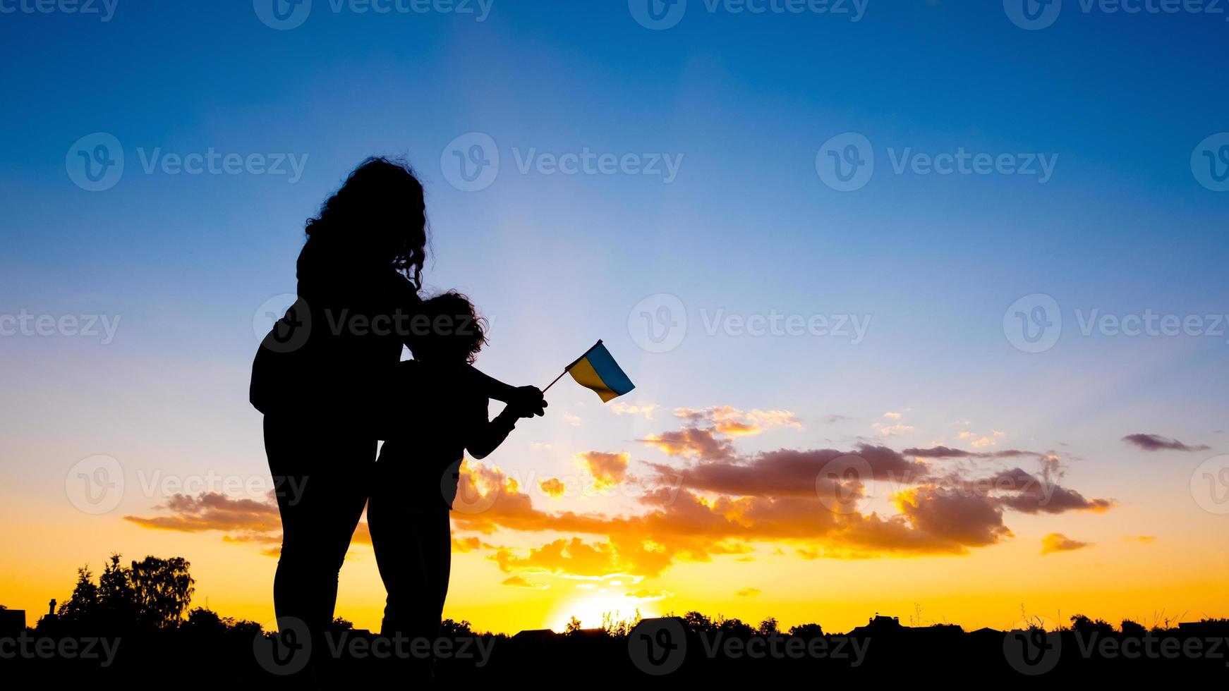 madre con un' bambino contro il sfondo di un' blu giallo tramonto cielo con il bandiera di Ucraina nel mano, ucraino vittoria nel il guerra foto