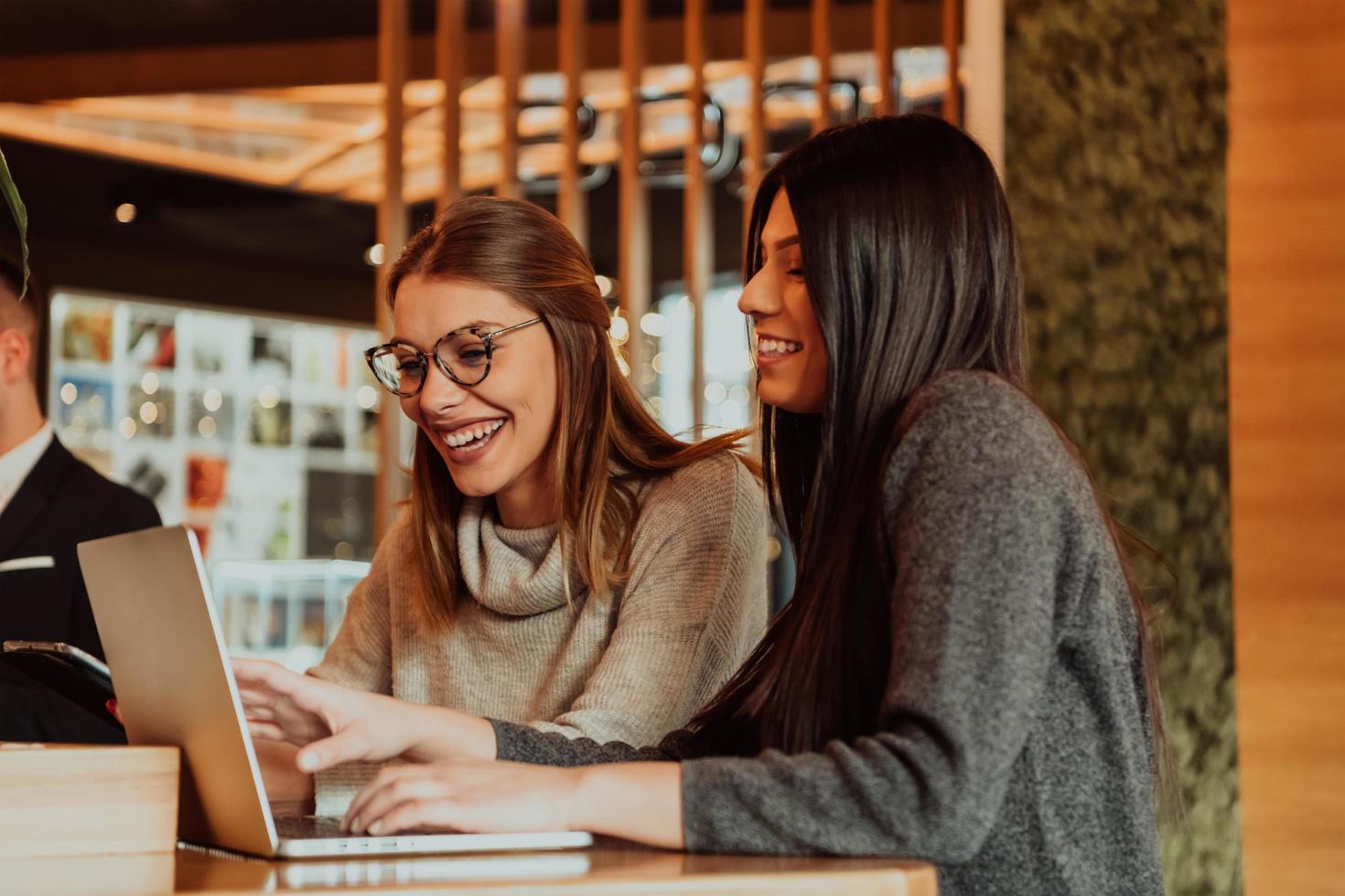 Due giovane attività commerciale donne seduta a tavolo nel bar. ragazza Spettacoli collega informazione su il computer portatile schermo. ragazza utilizzando smartphone, blogging. lavoro di squadra, attività commerciale incontro. foto