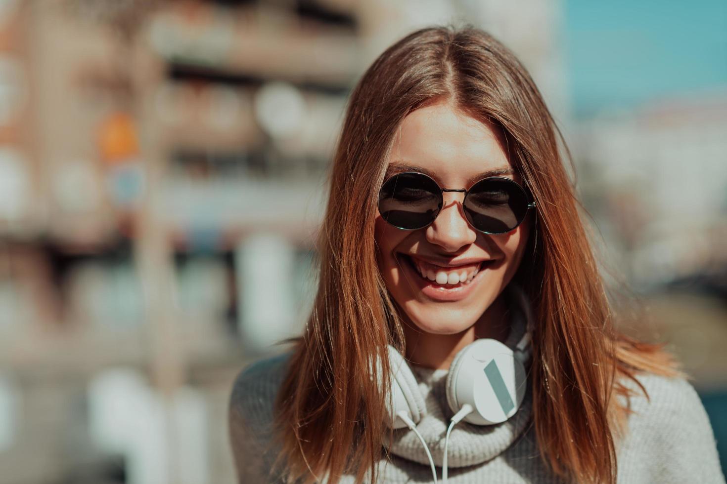 un' moderno ragazza con occhiali da sole a piedi giù il strada ascolta per musica nel cuffia. foto