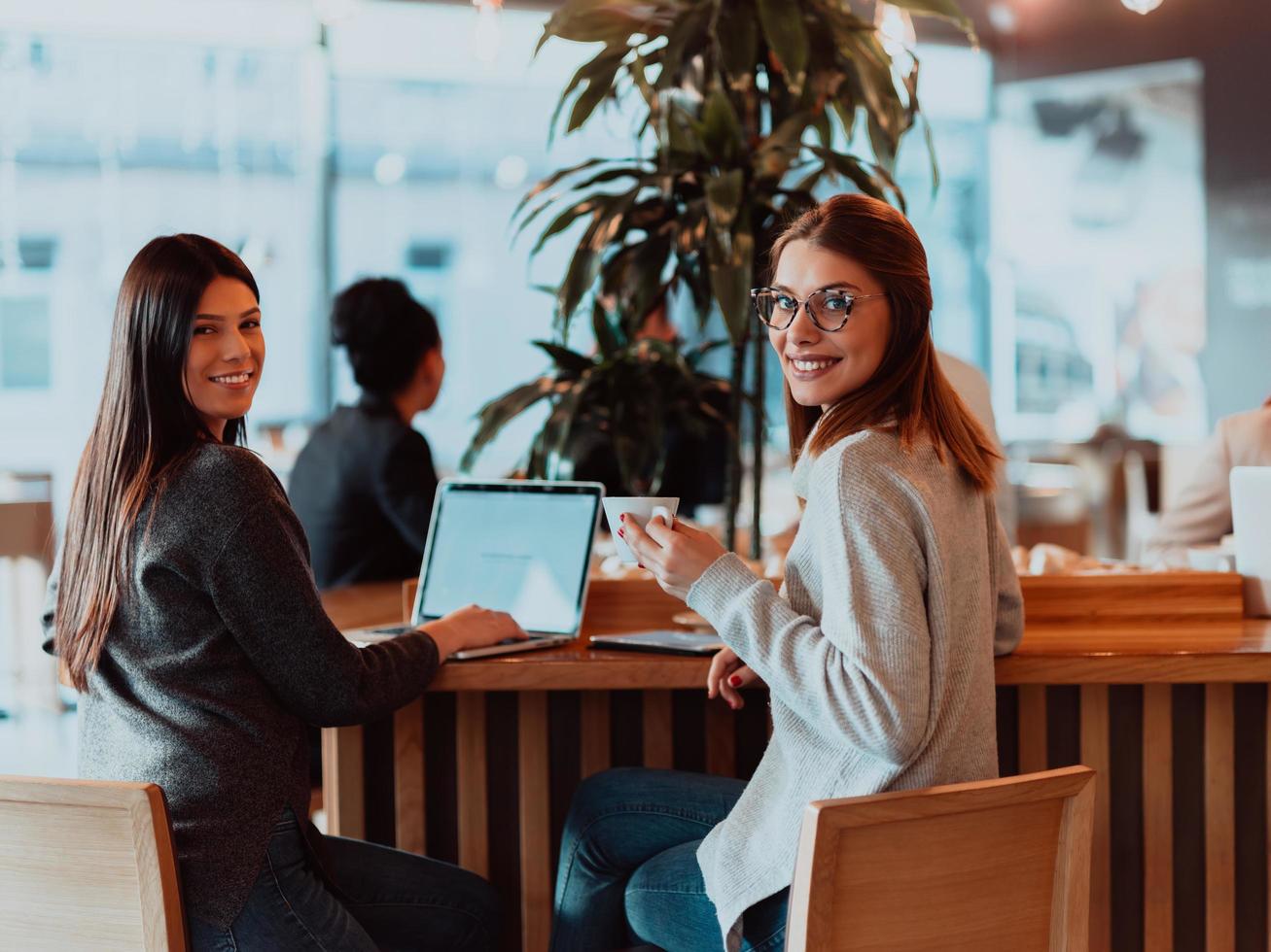 Due giovane attività commerciale donne seduta a tavolo nel bar. ragazza Spettacoli collega informazione su il computer portatile schermo. ragazza utilizzando smartphone, blogging. lavoro di squadra, attività commerciale incontro.. foto