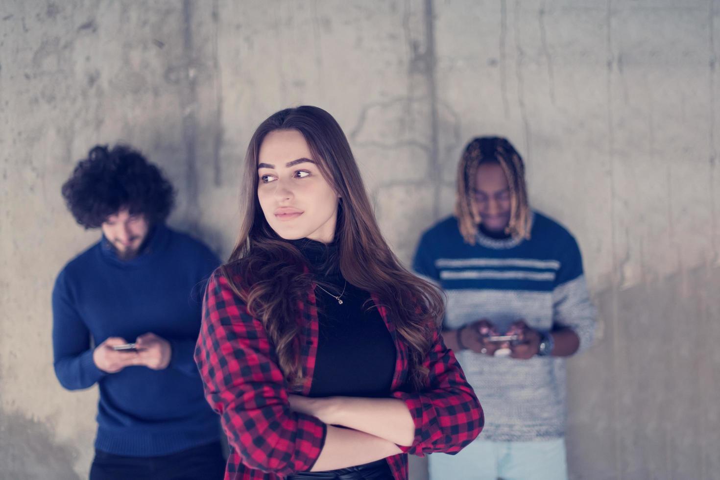 casuale multietnico attività commerciale squadra utilizzando mobile telefoni nel davanti di un' calcestruzzo parete foto