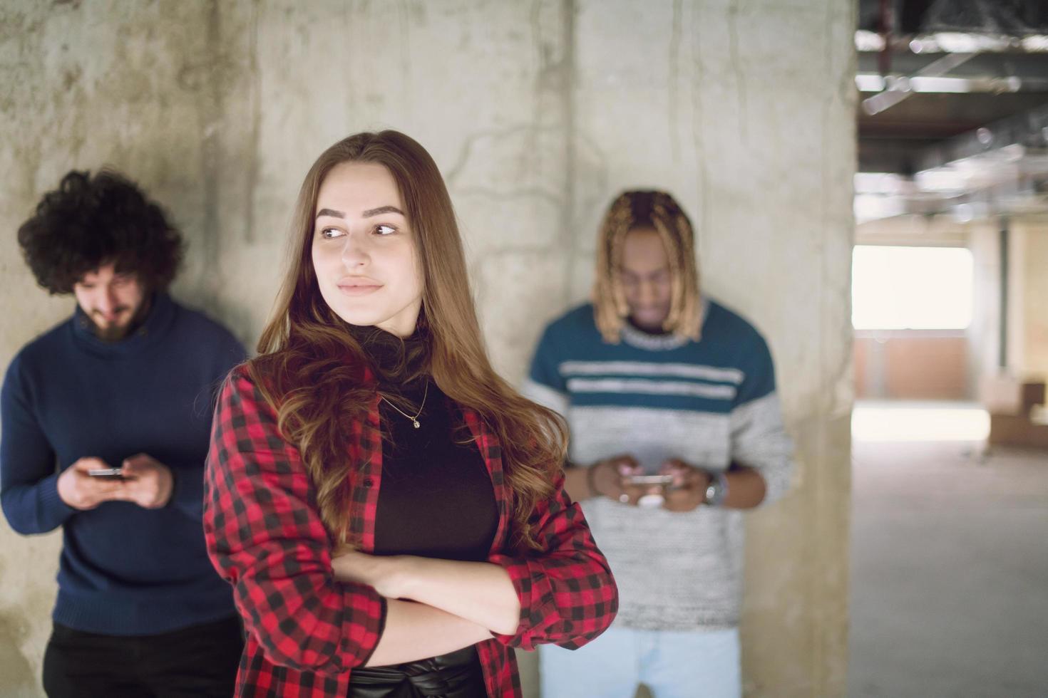 casuale multietnico attività commerciale squadra utilizzando mobile telefoni nel davanti di un' calcestruzzo parete foto