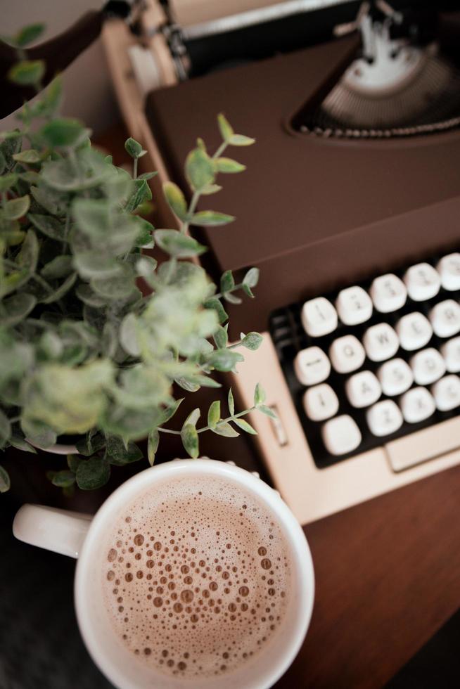 primo piano di una tazza di caffè vicino a una macchina da scrivere e una pianta foto