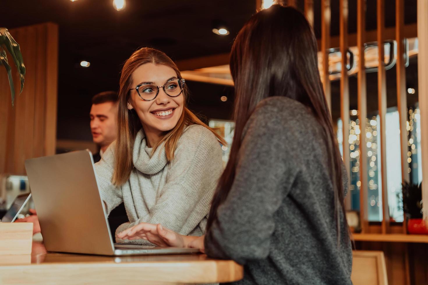 Due giovane attività commerciale donne seduta a tavolo nel bar. ragazza Spettacoli collega informazione su il computer portatile schermo. ragazza utilizzando smartphone, blogging. lavoro di squadra, attività commerciale incontro. foto